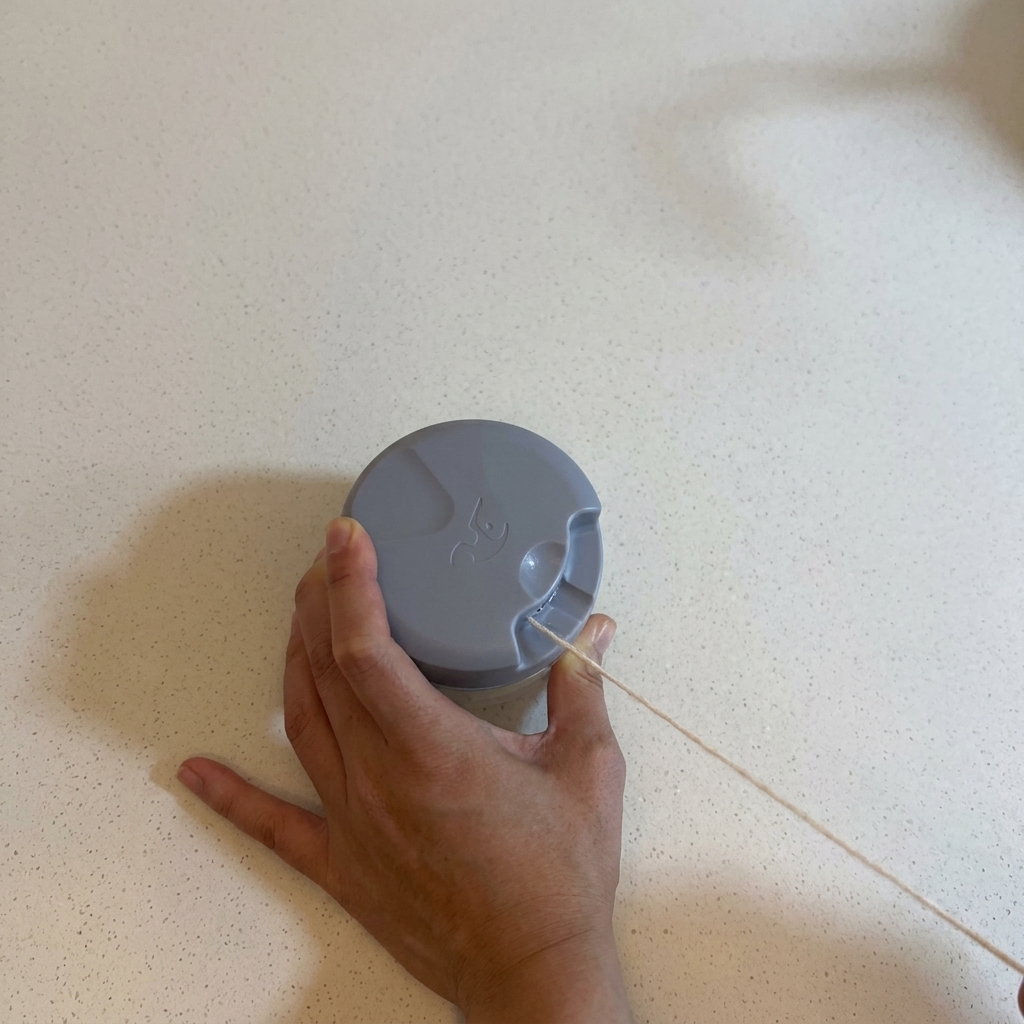 Hands operating a manual pull chopper on a white countertop to mince garlic.