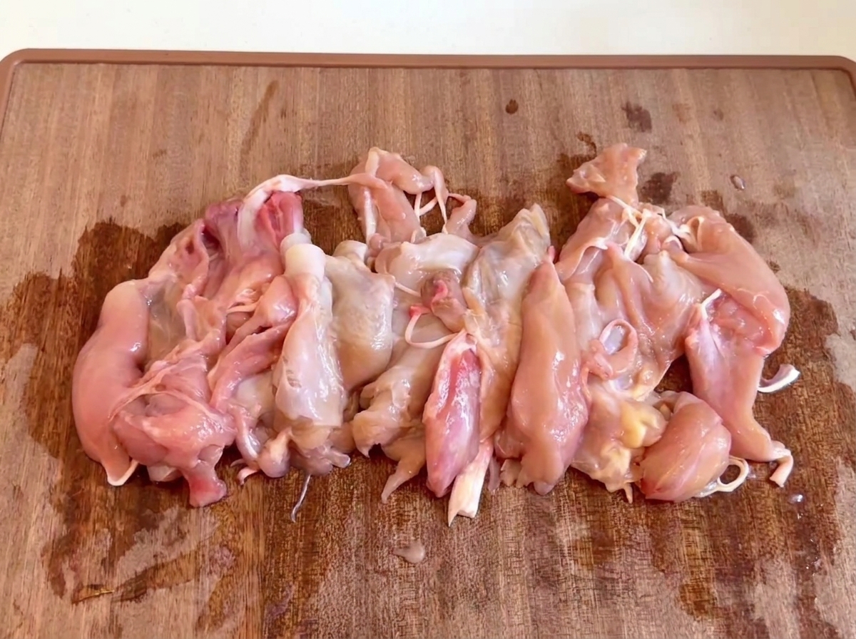 Raw, de-boned chicken meat pieces gathered together on a wooden cutting board.