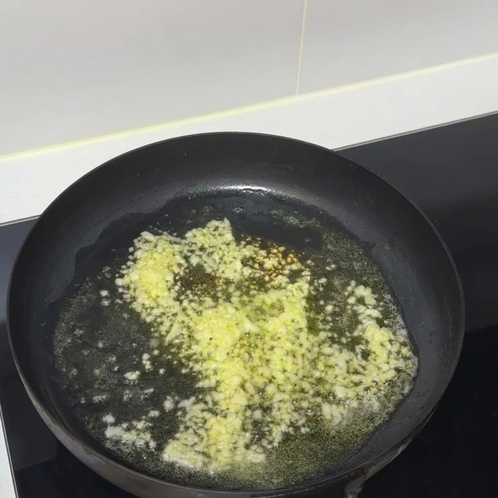 Minced garlic and melted butter sizzling together in a black non-stick frying pan.