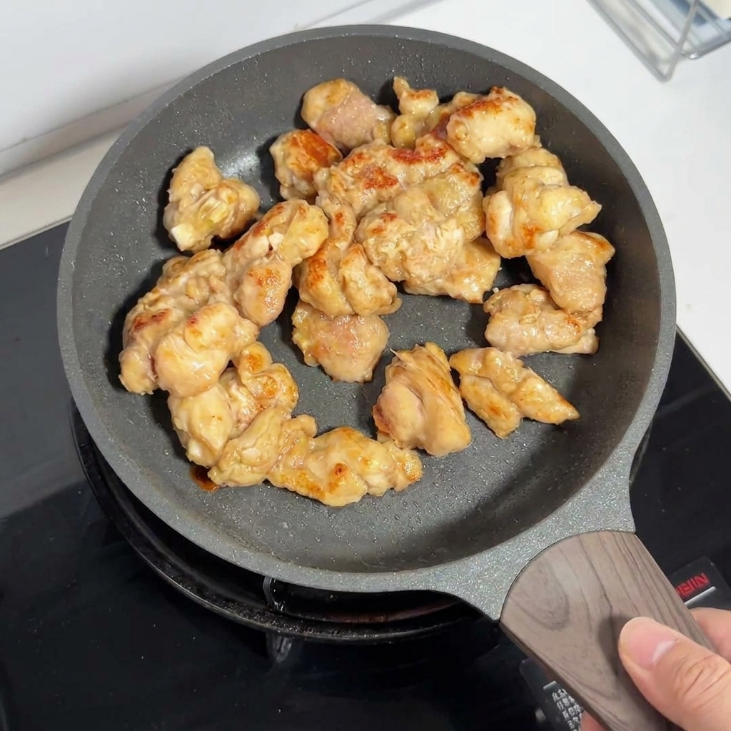 Golden-brown chicken thigh pieces frying inside a non-stick pan.