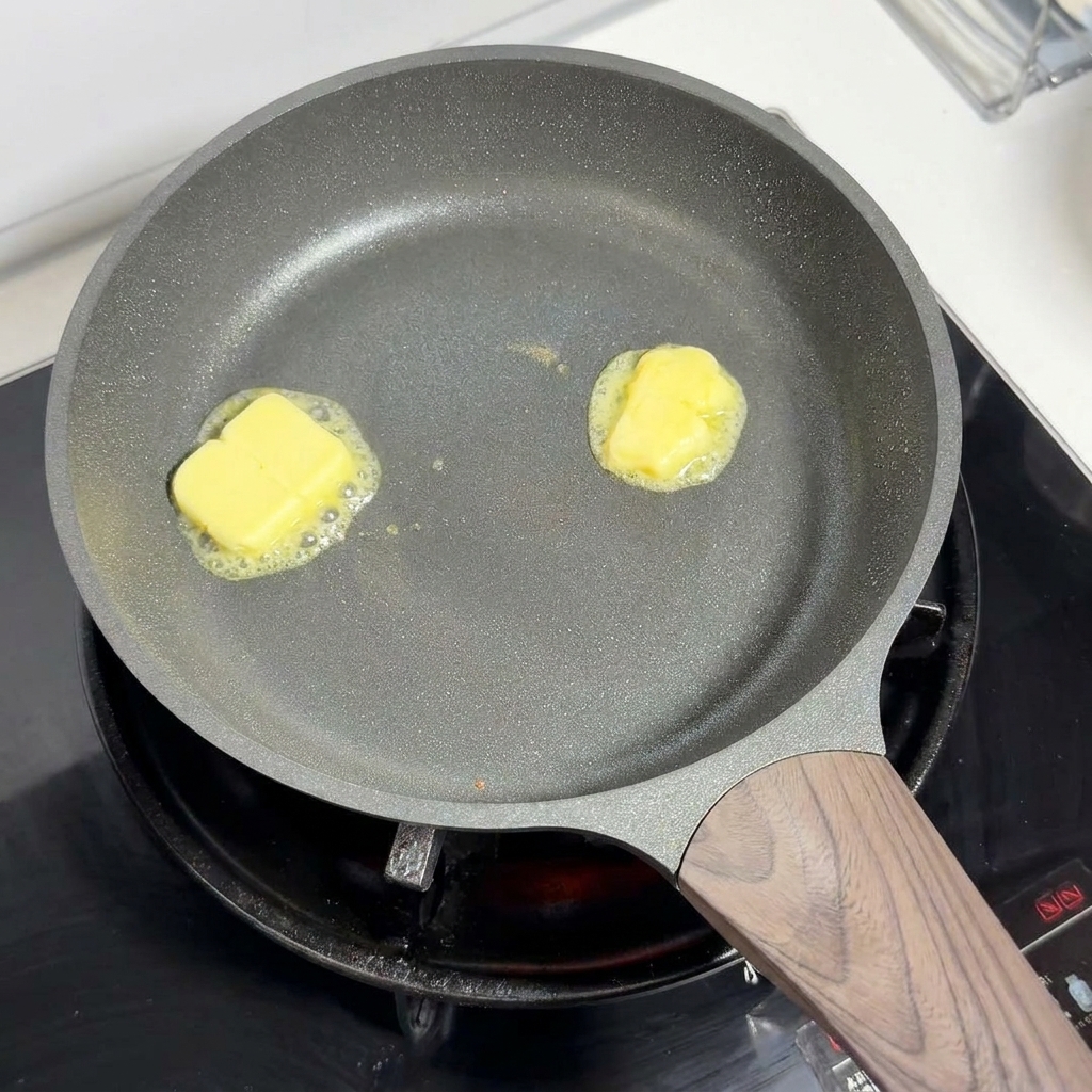 Two squares of yellow butter melting and bubbling in a pan on low heat.