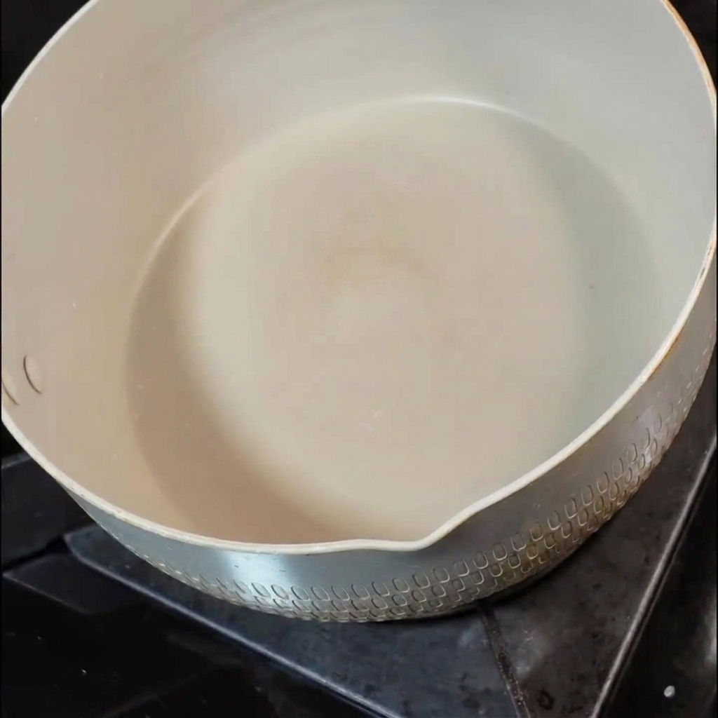 A small pat of butter melting inside a white ceramic pan on a stovetop burner.
