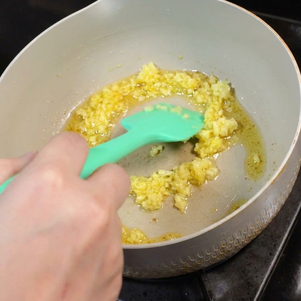 Minced garlic frying in melted butter in a pan, stirred with a green silicone spatula.