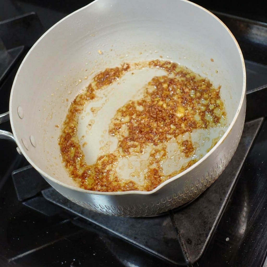 A small ladle of savory noodle broth being poured into the aromatic garlic butter mixture.