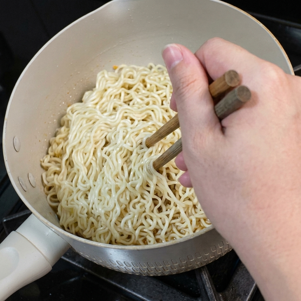 Wooden chopsticks tossing a mound of noodles inside the pan to coat them with the sauce.