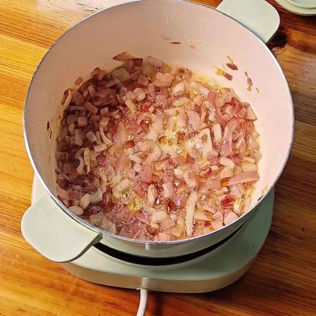 Sautéed diced red onions in a pot with minced garlic and ginger being mixed together.