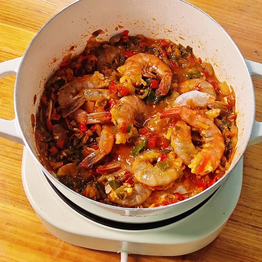 Clear water being poured from a small bowl into a pan with shrimp and sauce.