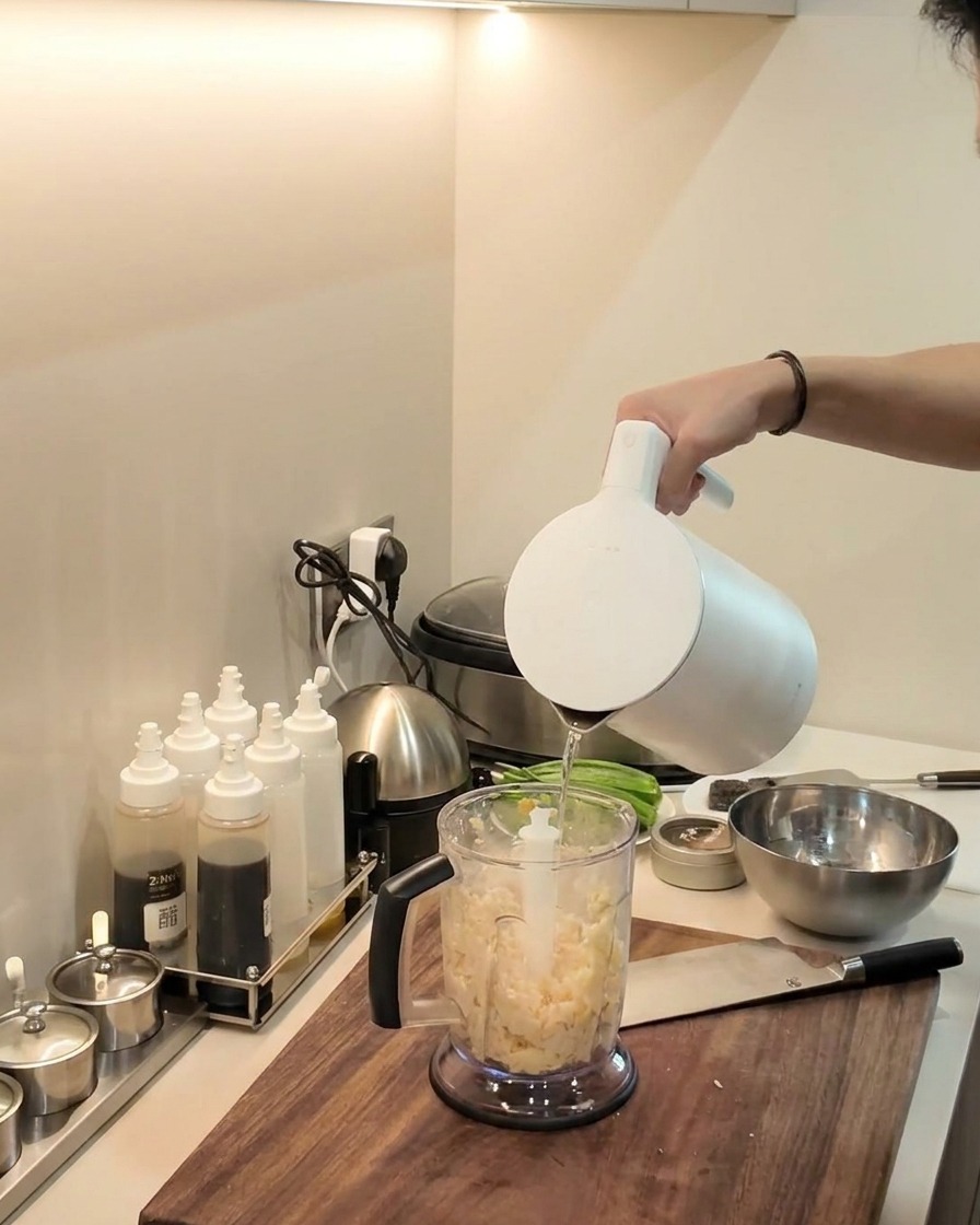 An immersion blender pureeing the cassava and plantain mixture inside the blender pitcher.