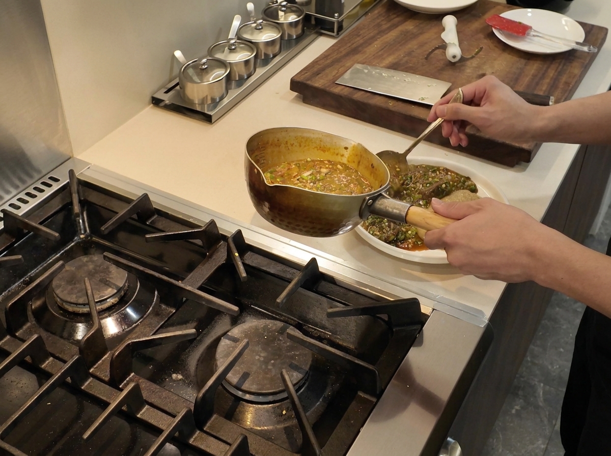A ladle pouring steaming hot okra and fish stew onto a white plate alongside a square portion of fufu.