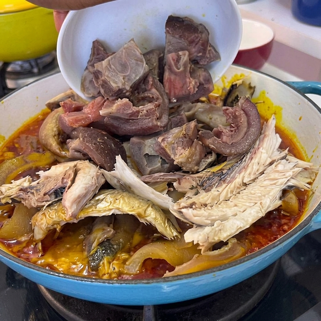 Cooked pork meat pieces being poured from a bowl into the pot containing fish and sauce.