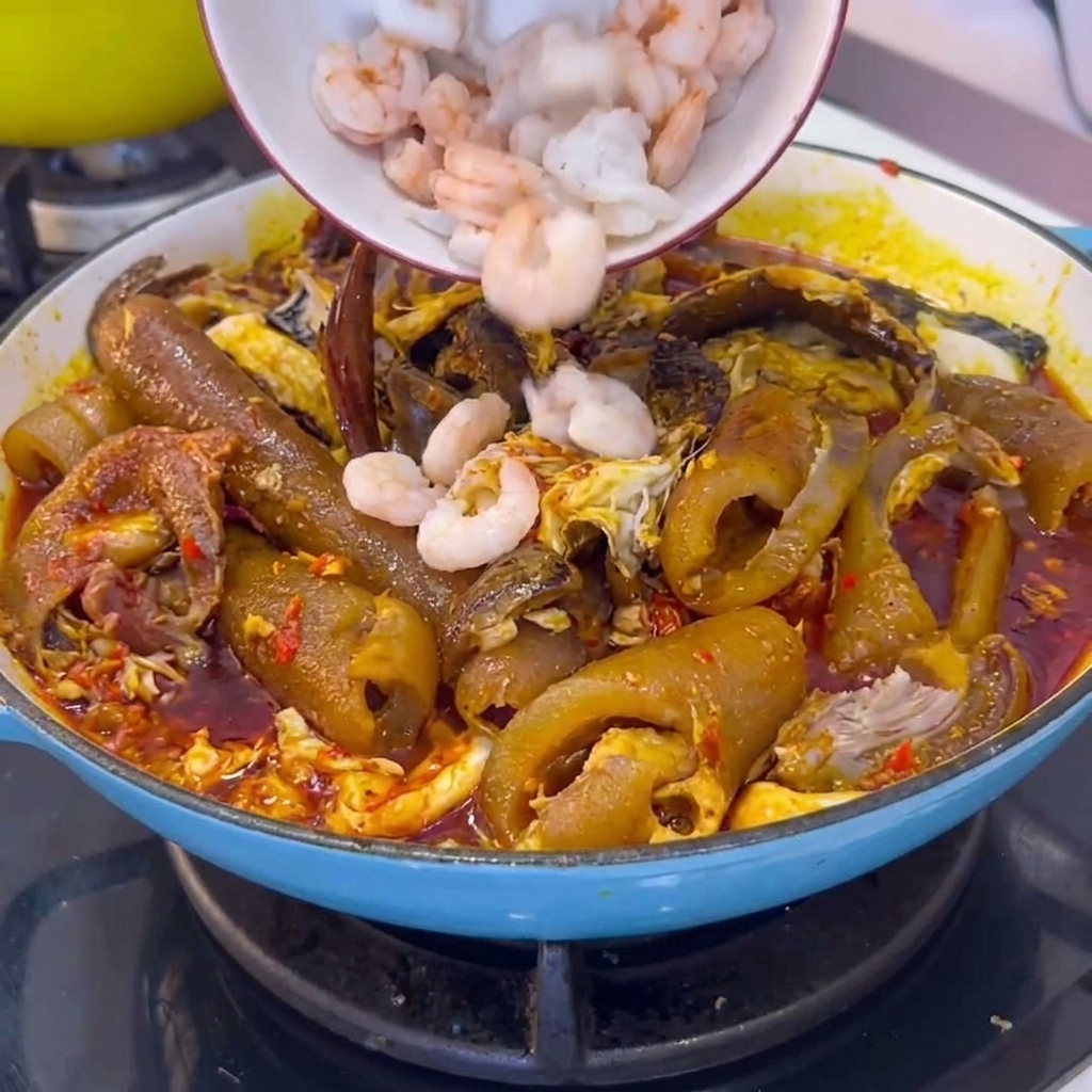 A bowl of peeled white shrimp being added into a cooking pot filled with braised pork skin and chili sauce.