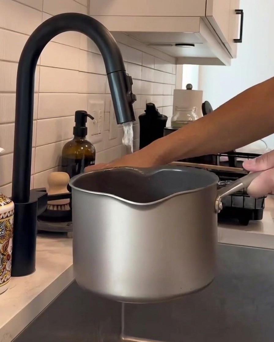 Hands stirring white rice inside a metal pot under a running kitchen faucet.
