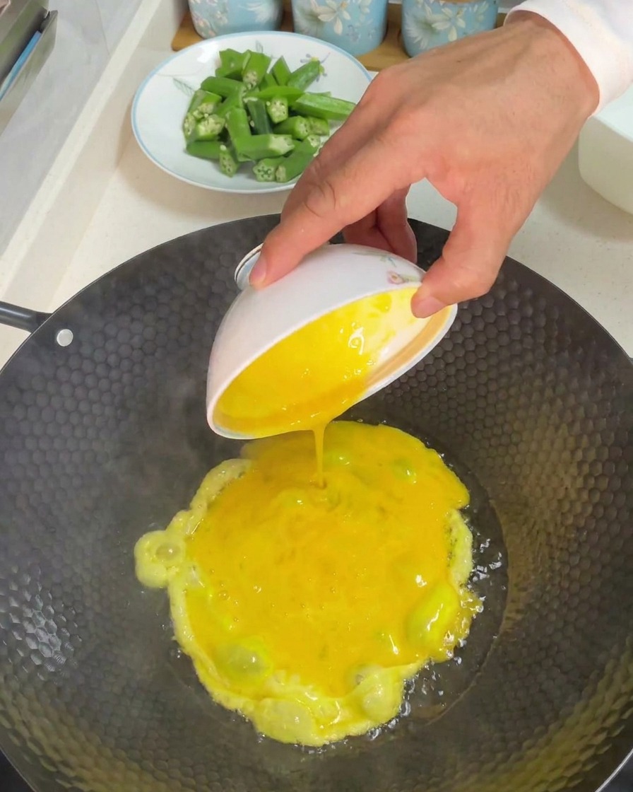 Pouring a bowl of beaten yellow eggs into a hot wok with oil.