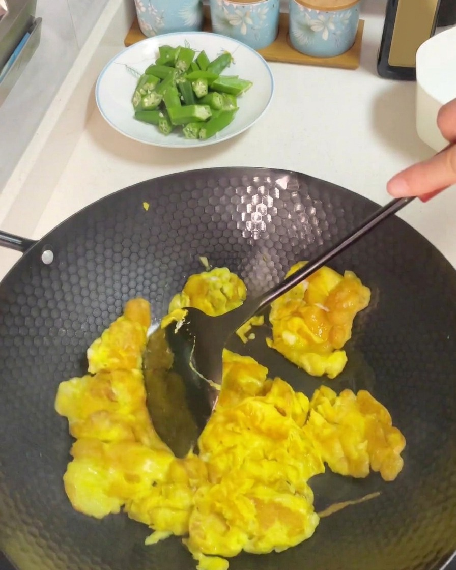 Using a dark spatula to stir and scramble cooked eggs in a heated wok.