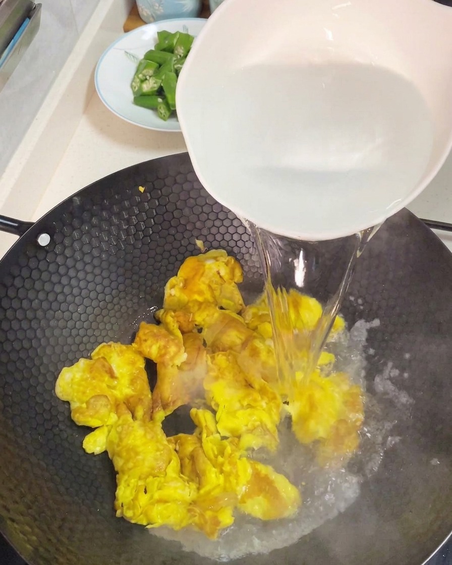 Pouring boiling hot water from a large white bowl over scrambled eggs to create a soup base.