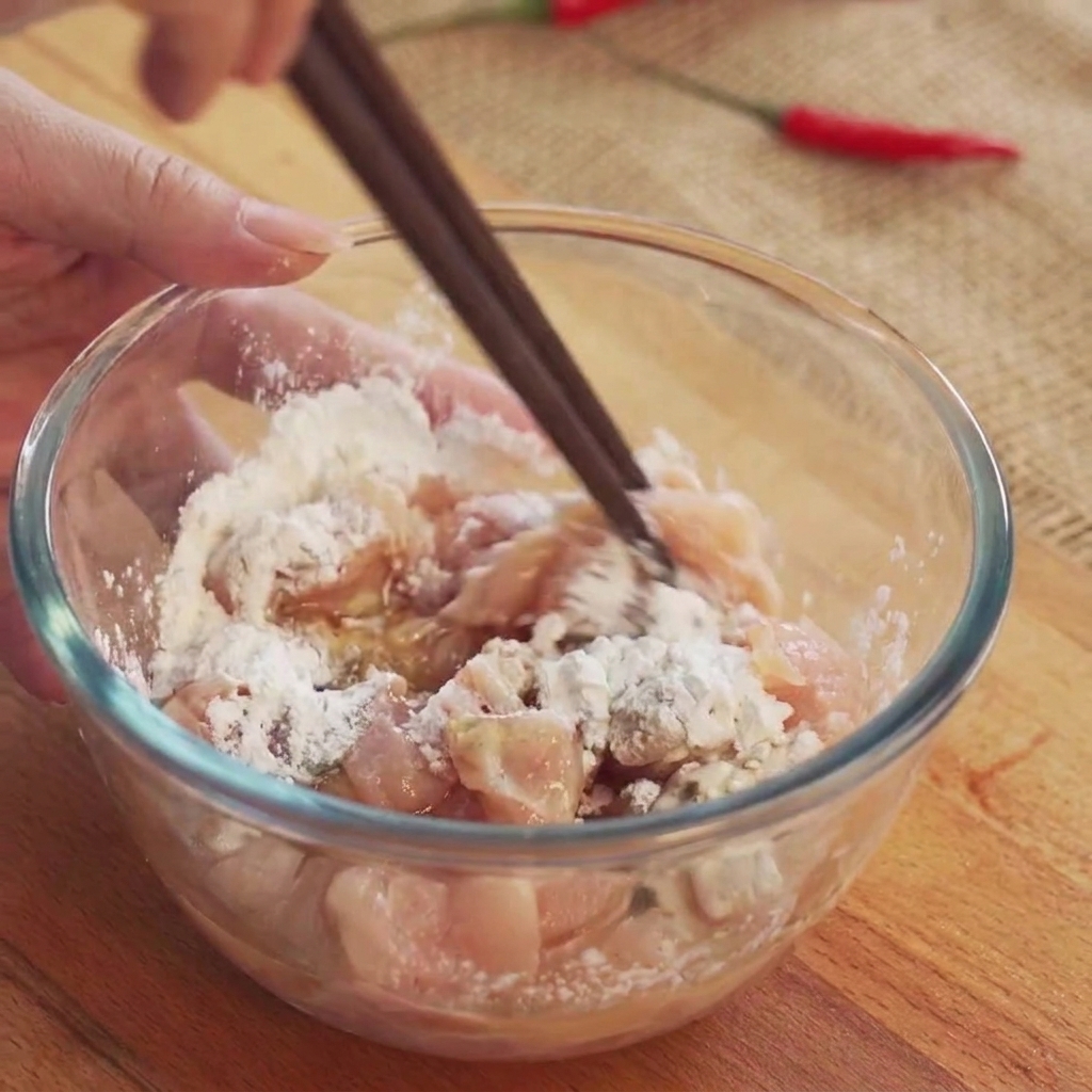 Chicken cubes being stirred with chopsticks inside a transparent glass bowl to mix the marinade.