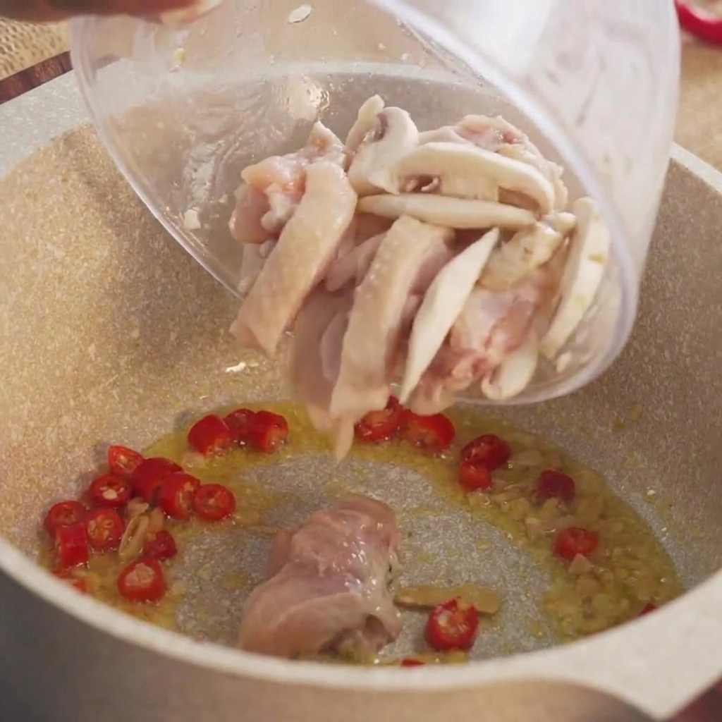 Marinated chunks of raw chicken being poured from a bowl into the hot pot.