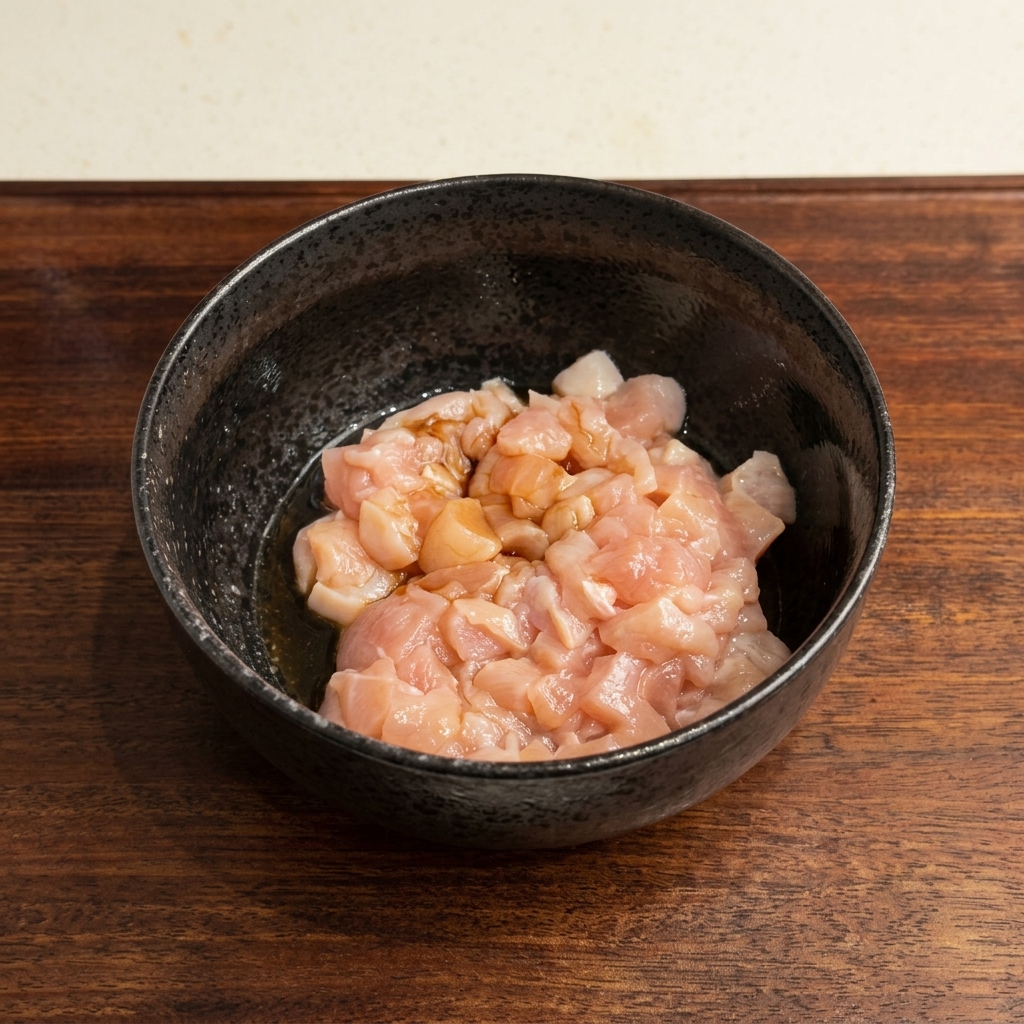 Raw diced chicken sitting in a black bowl with soy sauce poured over it.