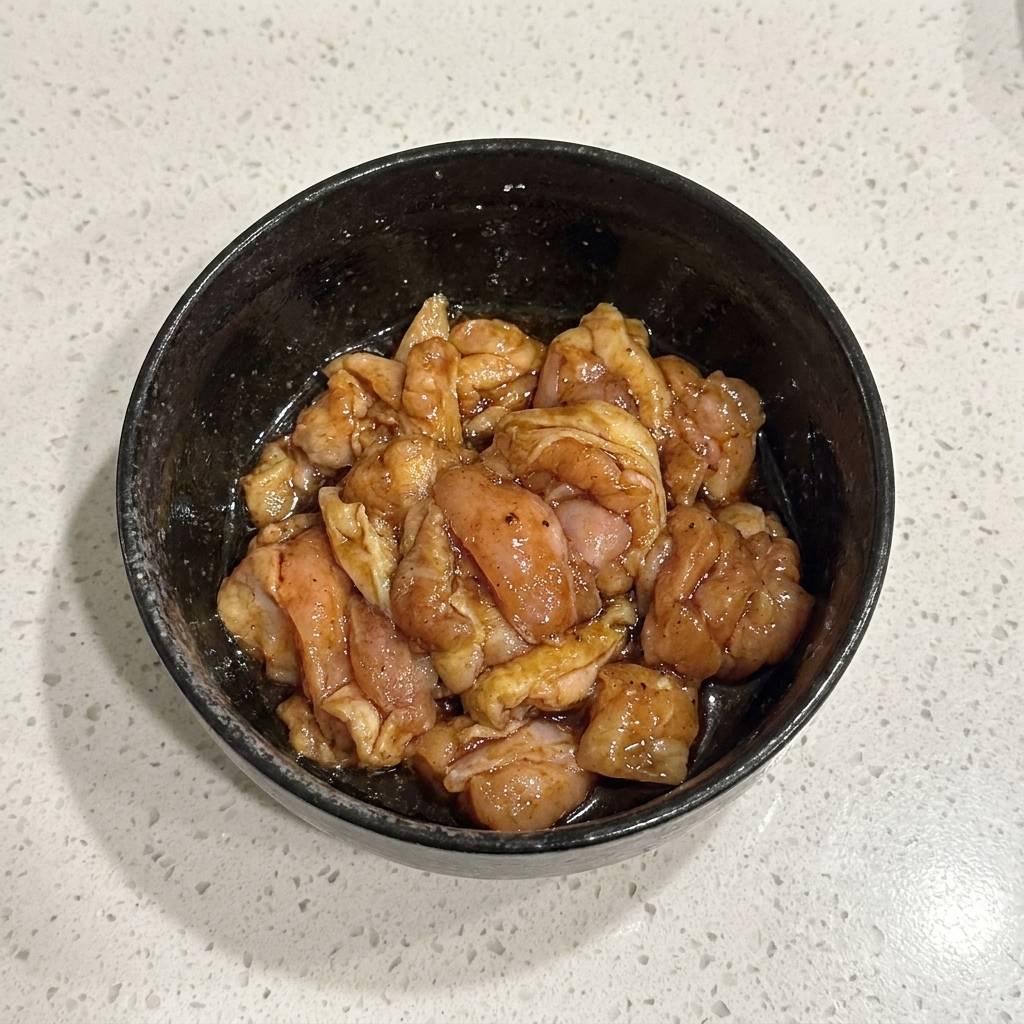 Marinated raw chicken pieces mixed thoroughly inside a black bowl.