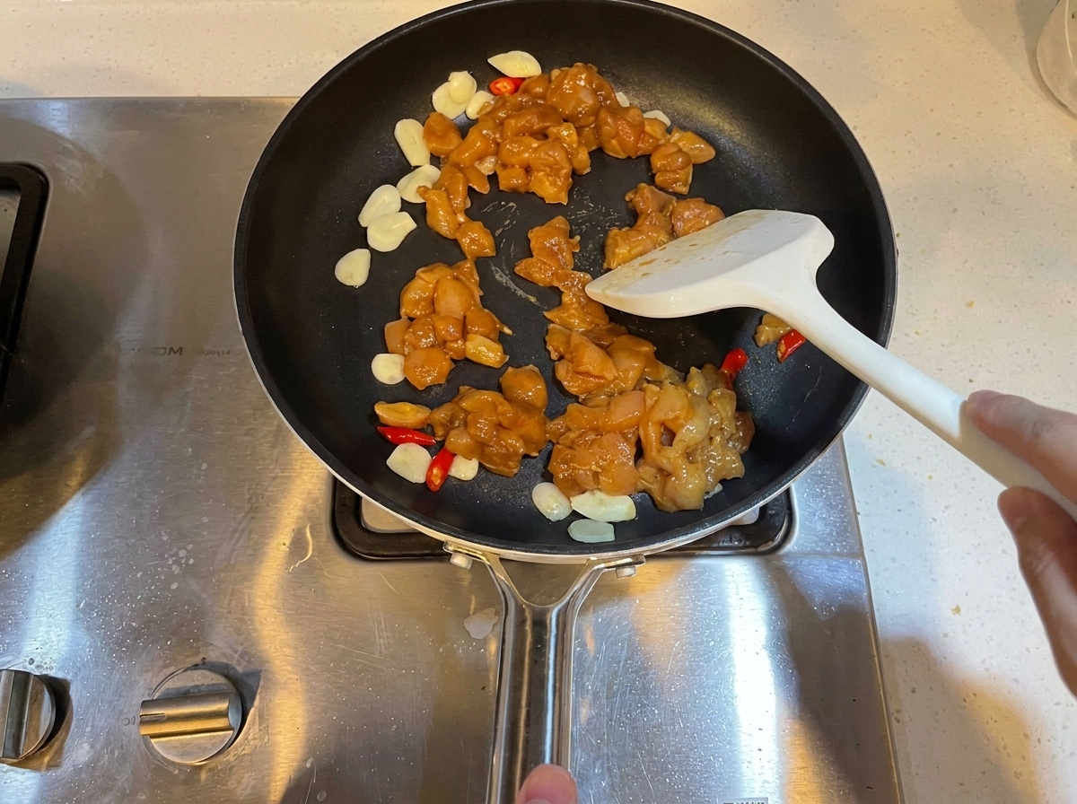 Marinated diced chicken pieces being stir-fried in a pan with garlic and chilies.