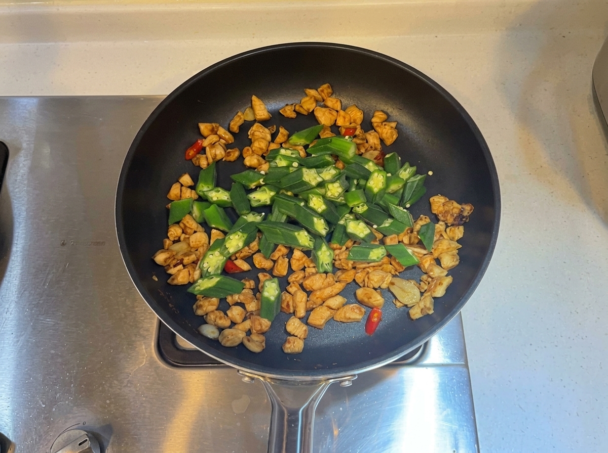 Green okra slices mixed into the pan with cooked chicken and aromatics.
