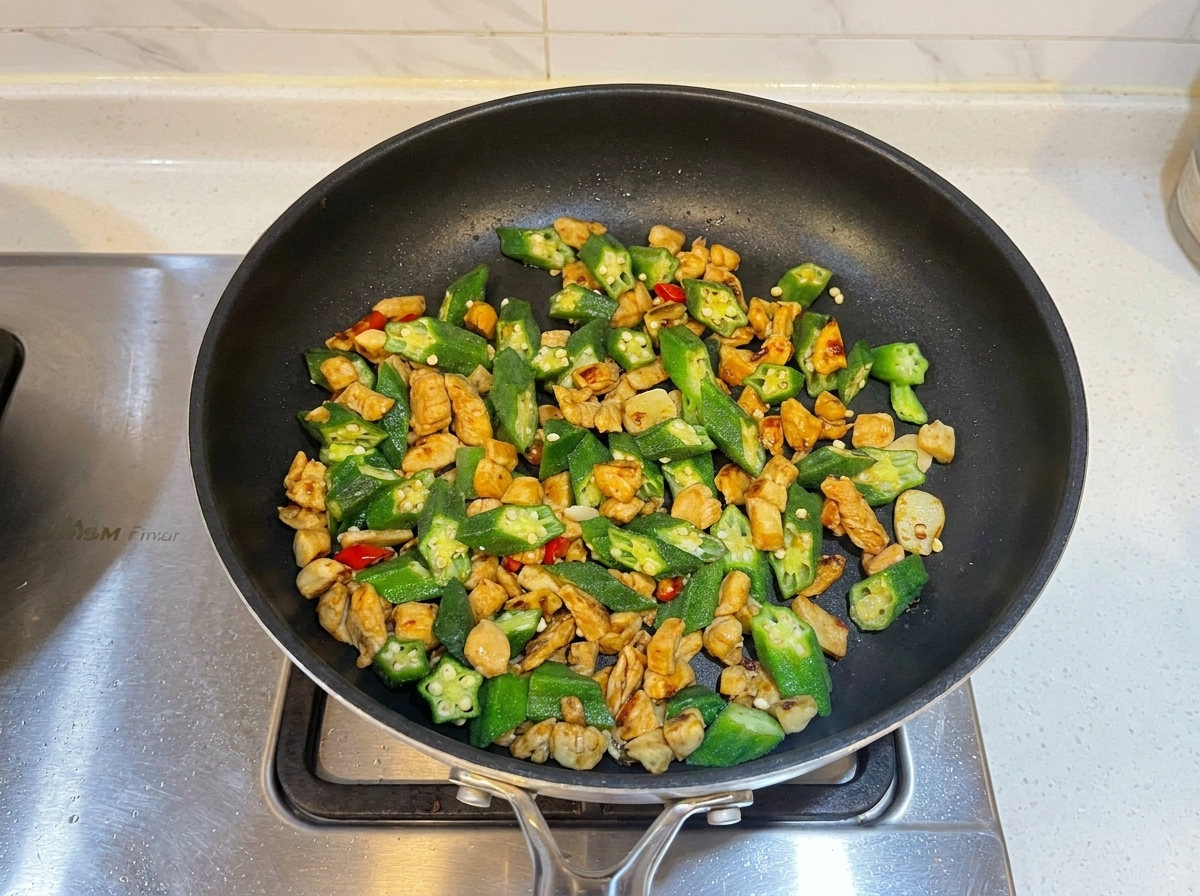 Oyster sauce being added to the chicken and okra stir-fry in the pan.