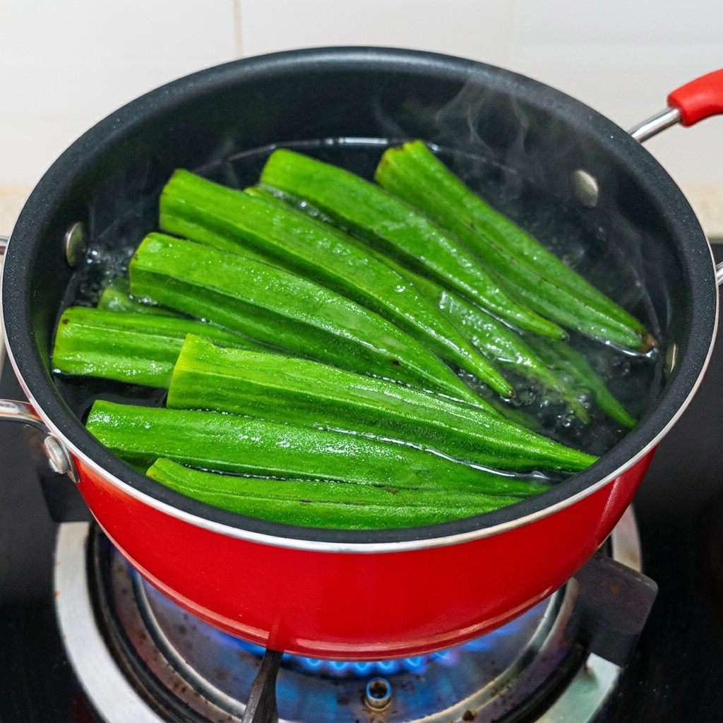 Green okra pods boiling vigorously in a red pot with seasoned water.