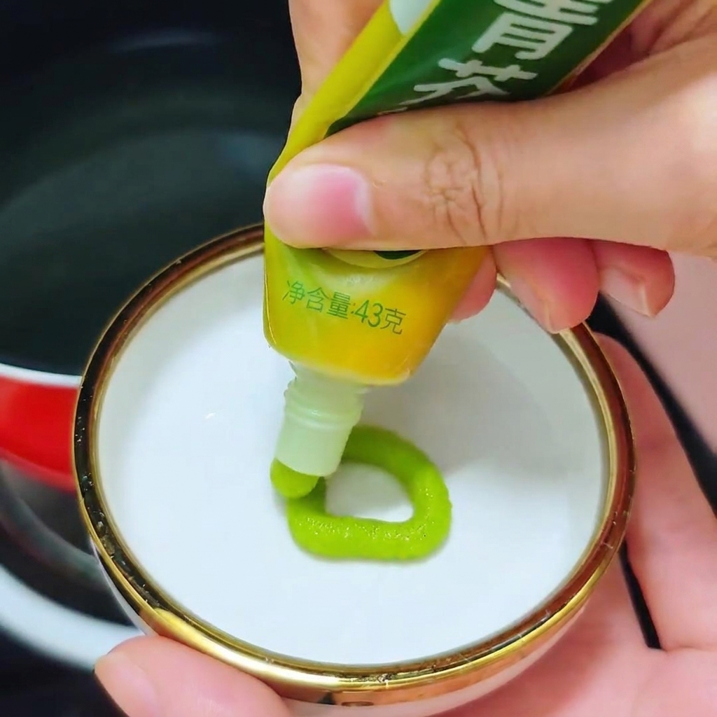 A person squeezing a ring of bright green wasabi paste from a tube into a small white dish.