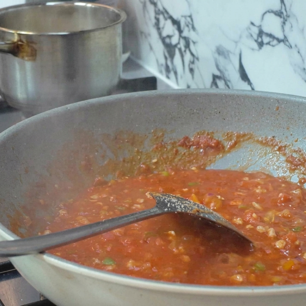 Fresh tomatoes being held on metal skewers and roasted directly over a bright blue kitchen gas burner flame.