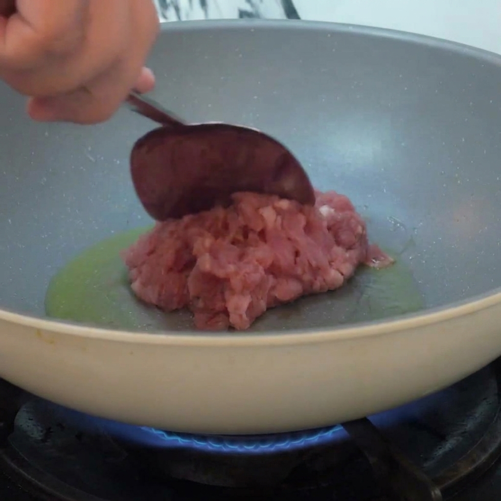 Minced meat being added to a pan with hot oil and stir-fried over a flame.