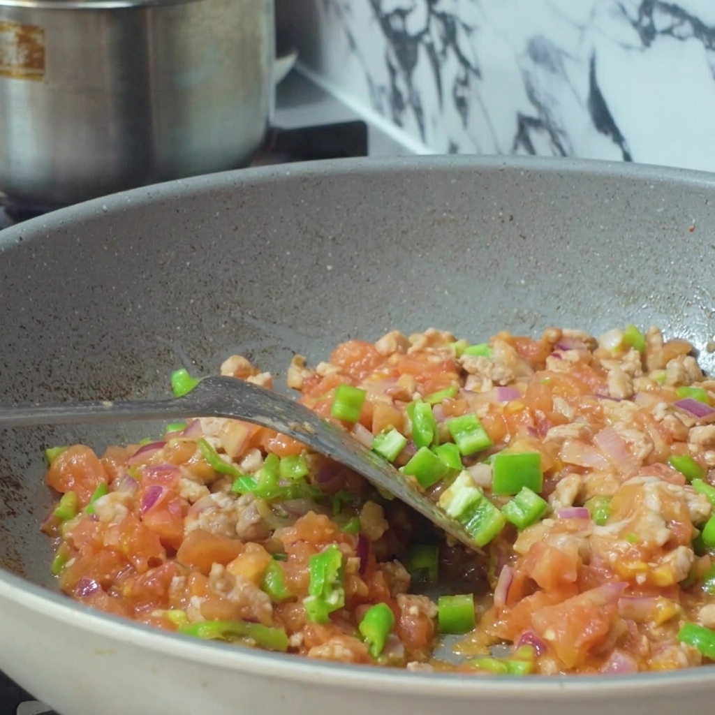 Water being poured from a container into a pan filled with a mixture of minced meat and diced vegetables.