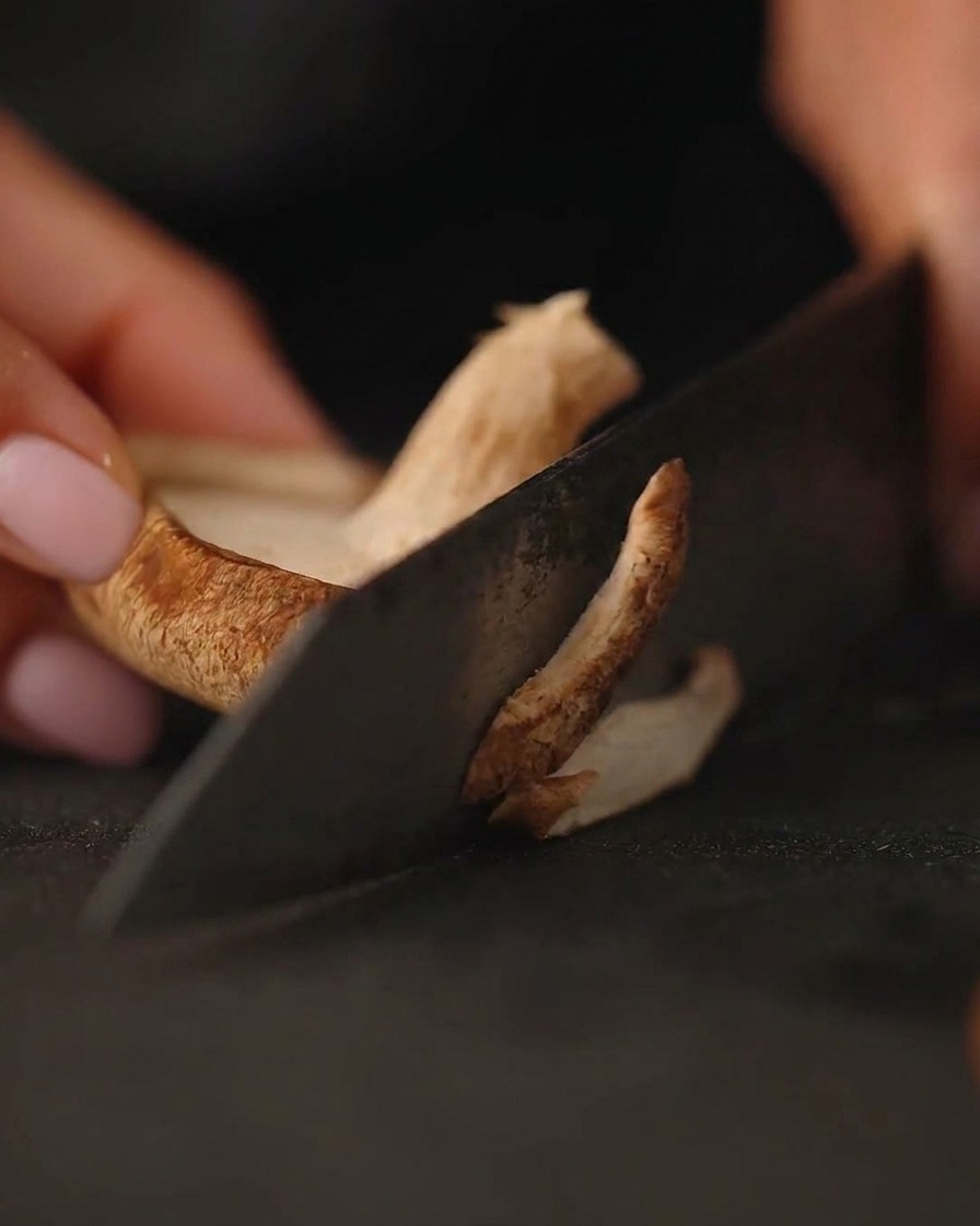 Close-up of fresh mushrooms being sliced on a dark cutting board with a knife.