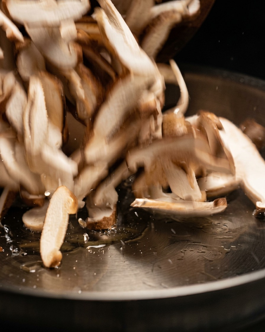 Raw mushroom slices being tossed and added into a hot cooking pan.