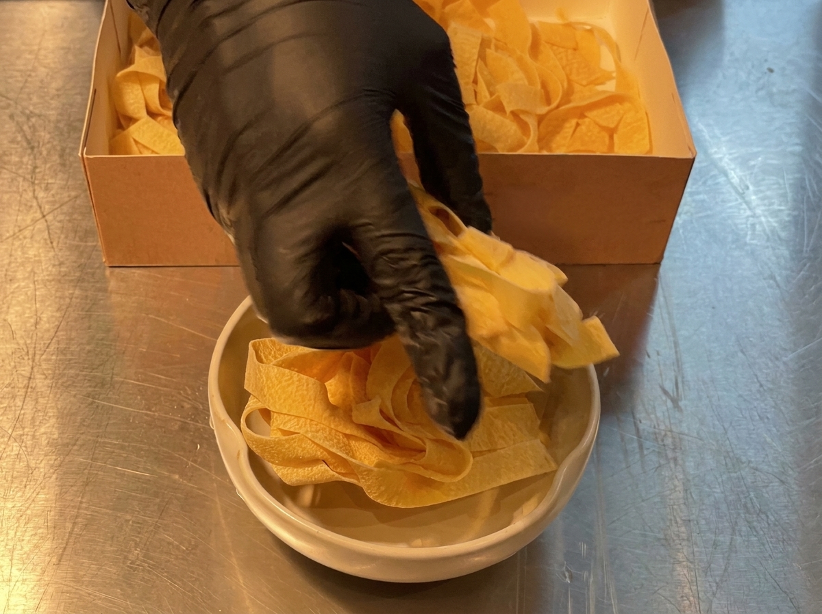 Wide pasta noodles being portioned out from a cardboard box into a cooking bowl.