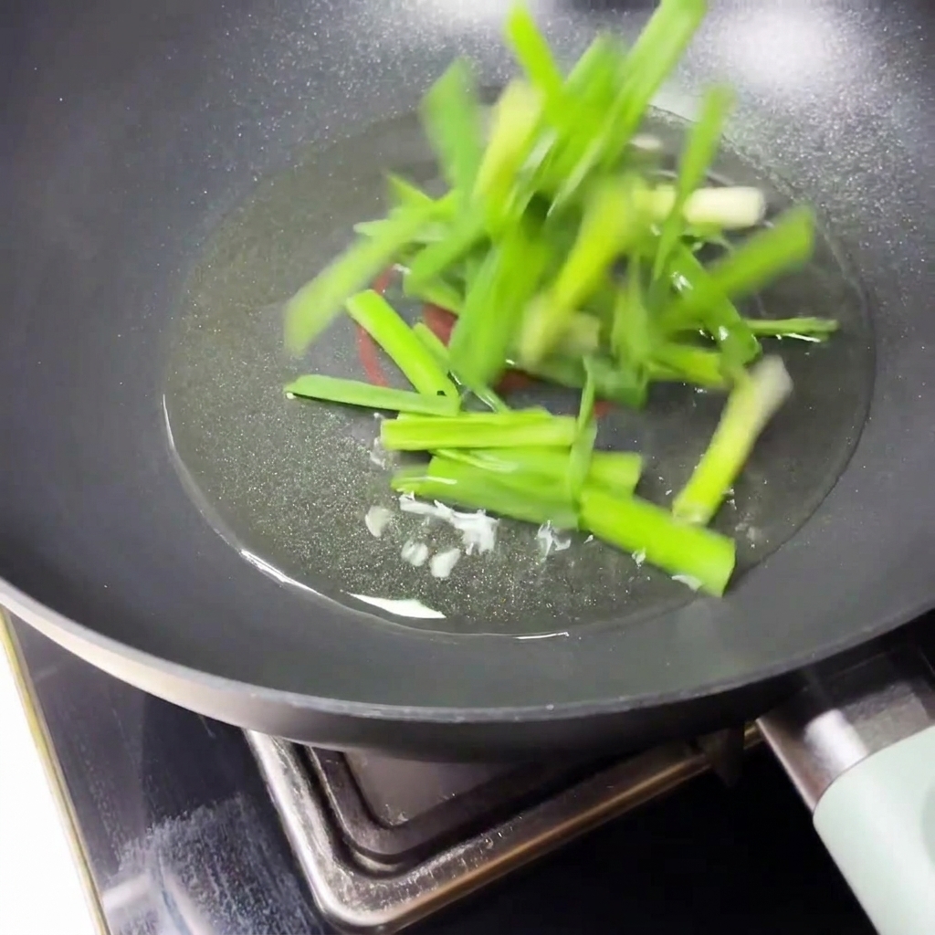 Sliced scallions being tossed and sautéed in hot oil inside a black frying pan.
