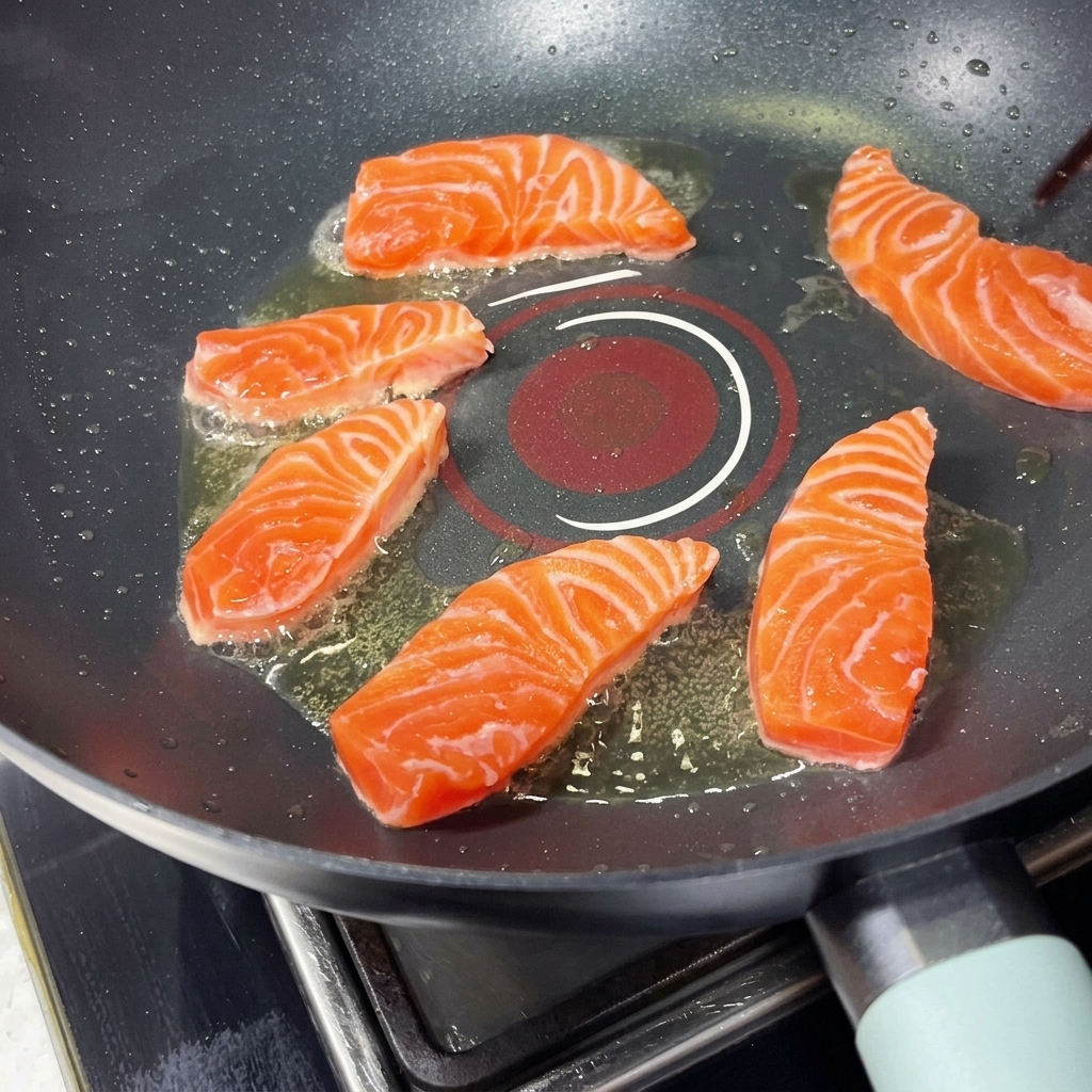 Several salmon pieces sizzling in a hot pan arranged in a circular pattern, being placed with chopsticks.