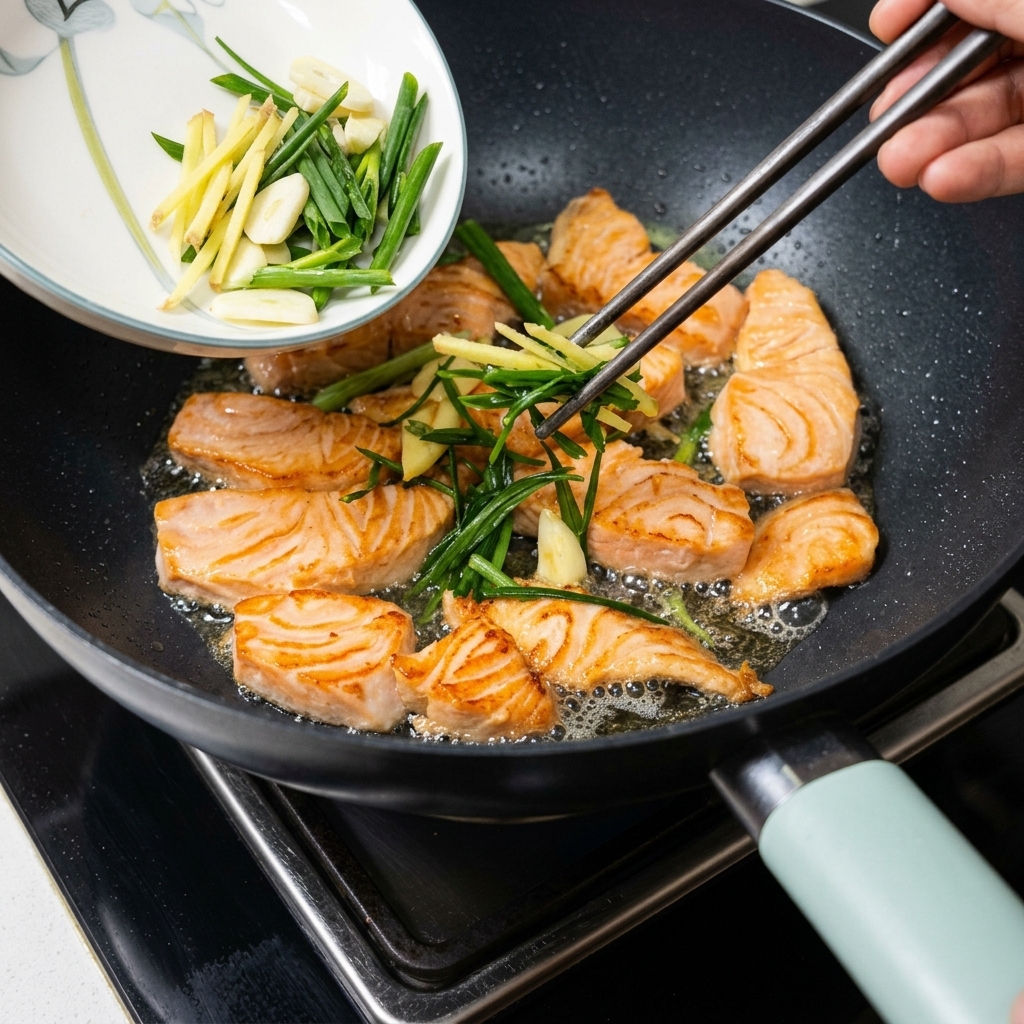 Sautéed scallions and ginger being poured from a small white dish into a frying pan with salmon pieces.