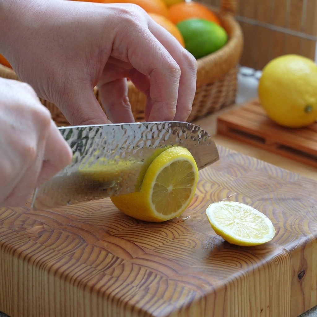 A yellow lemon being sliced into clean rounds on a wooden chopping board with a knife.