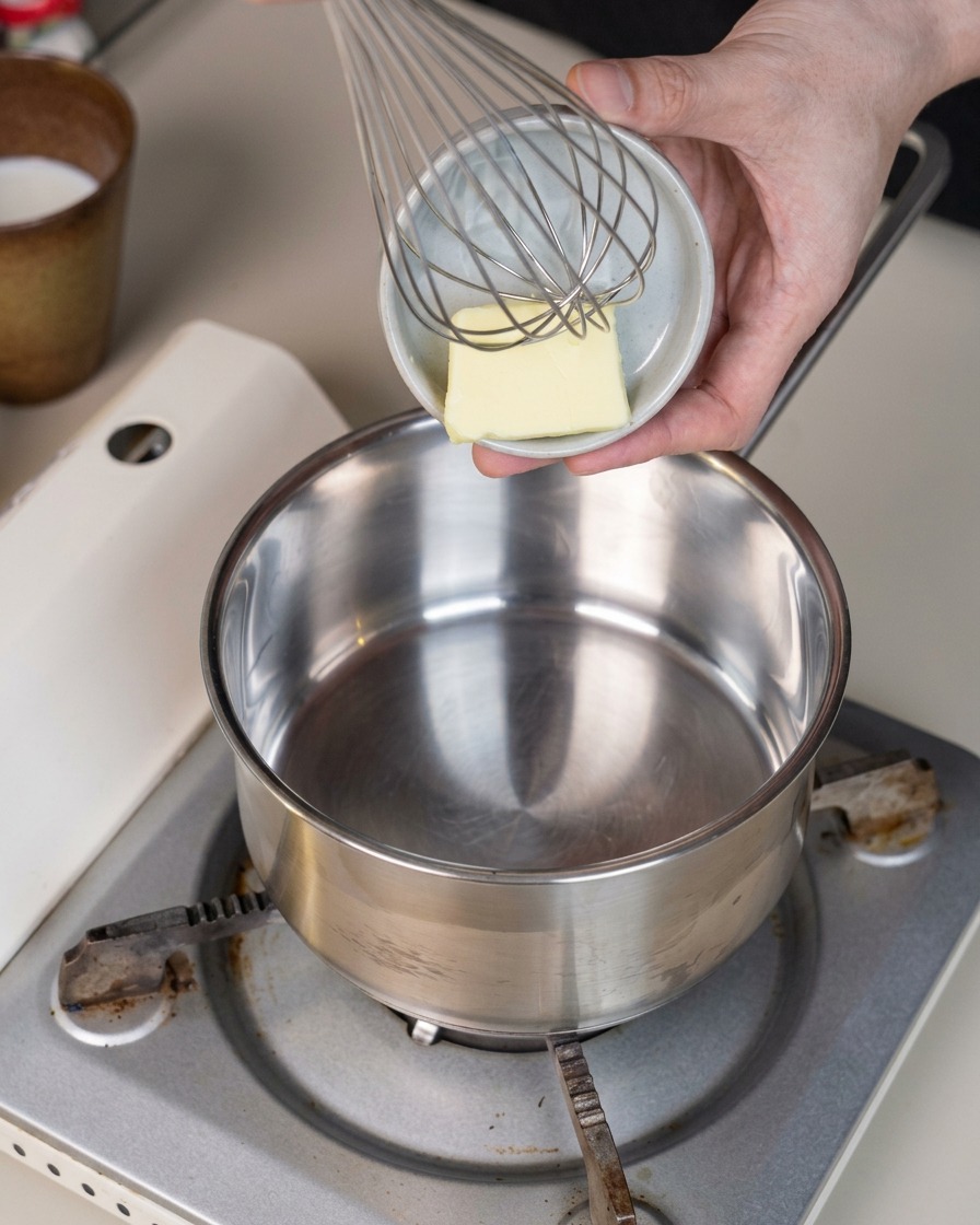 A small square of butter sitting inside a clean metal saucepan on a portable stove.