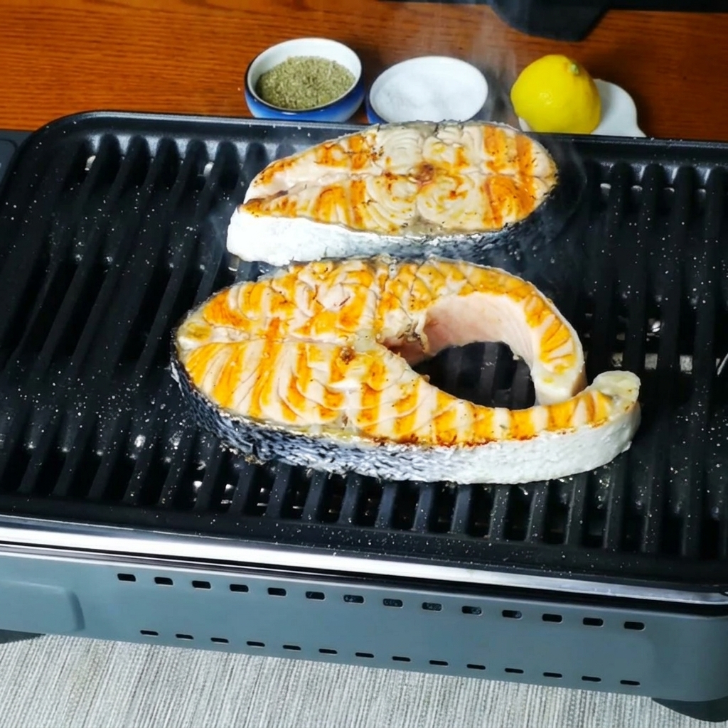 Close-up view of salmon steaks sizzling on the grill pan after being seasoned.
