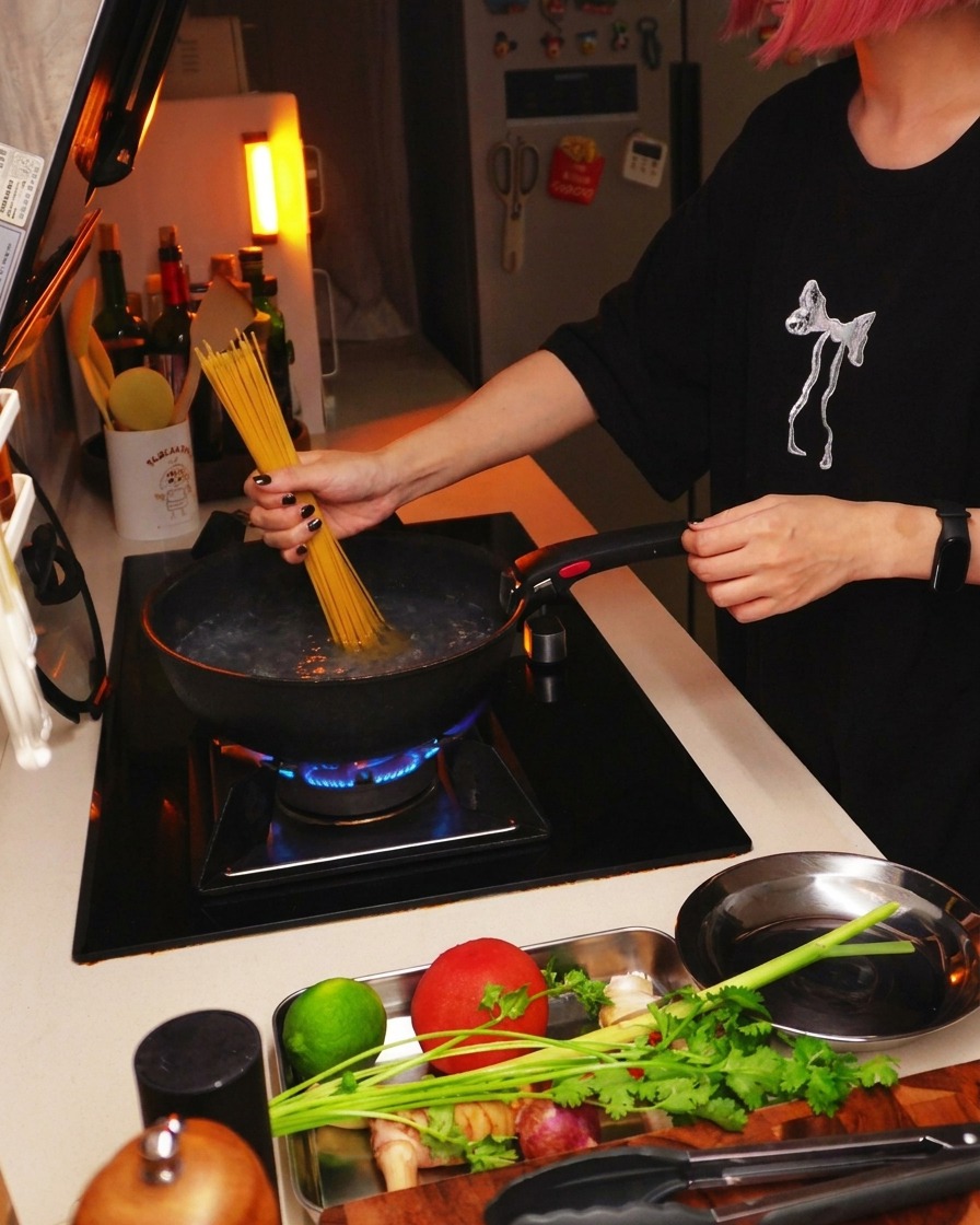 Dry spaghetti pasta being lowered into a pot of boiling water on a kitchen stove.