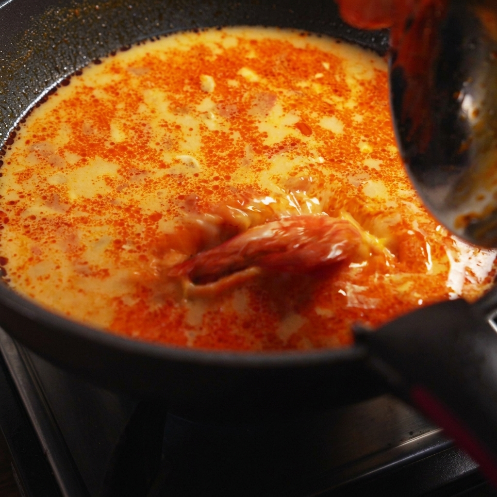 Cooked spaghetti noodles, prawns, and fresh coriander being tossed into the simmering pan of sauce.