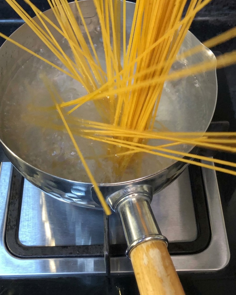 Spaghetti noodles being submerged into a pot of boiling salted water on a stovetopcite: 1.