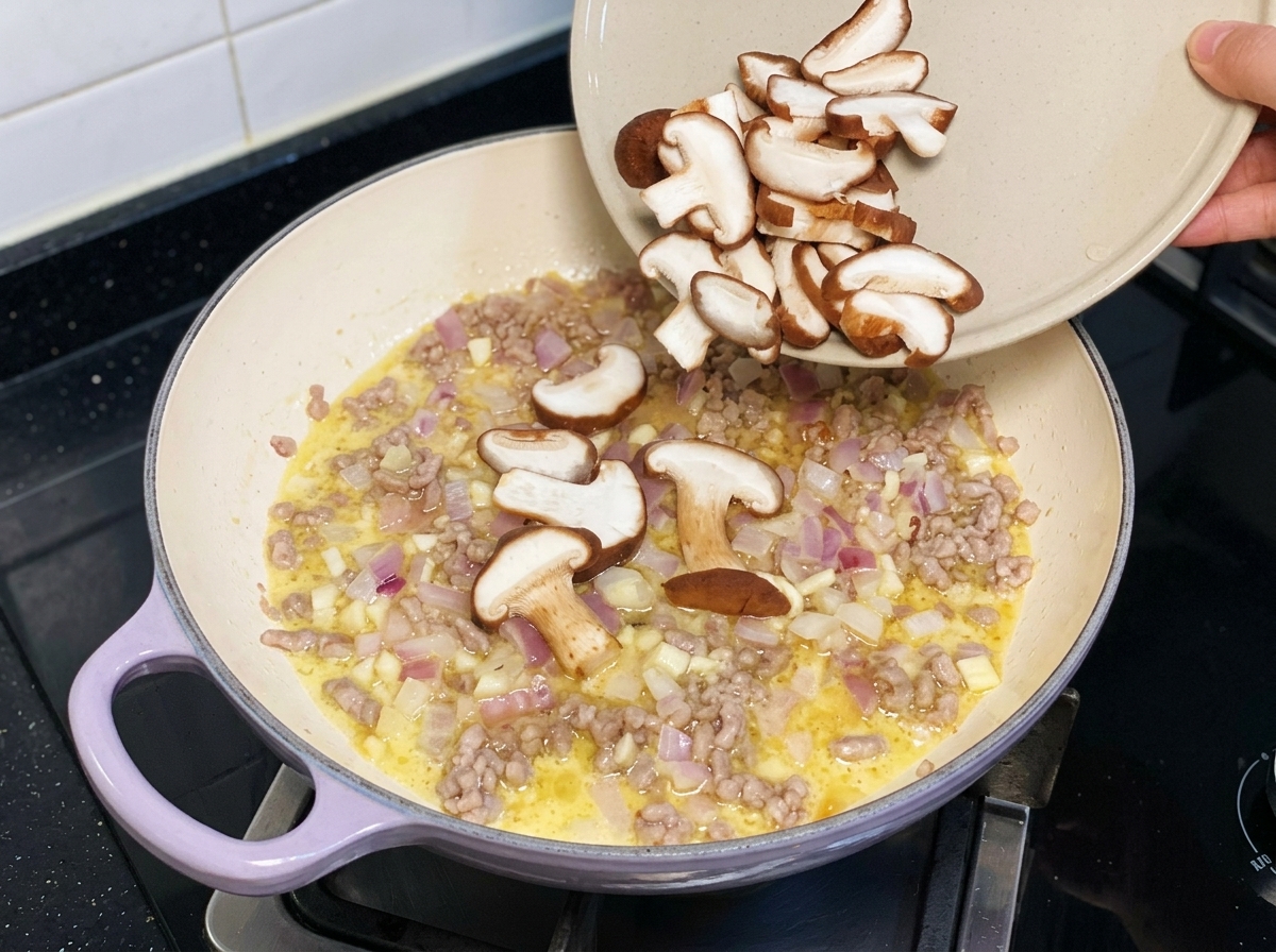 Sliced fresh shiitake mushrooms being poured from a plate into a pan with minced pork and onionscite: 1.