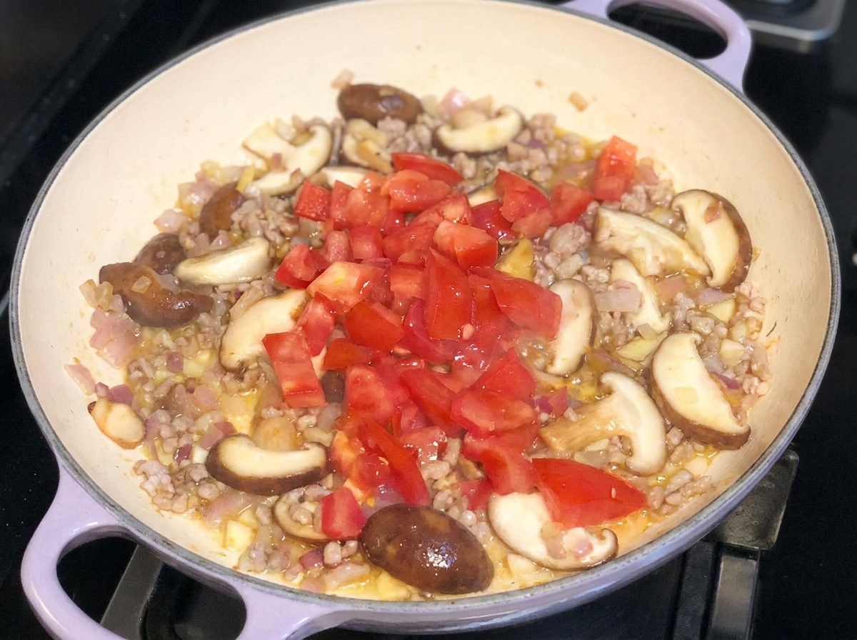 Freshly diced tomatoes added on top of a stir-fried mixture of pork, onions, and mushrooms in a pancite: 1.