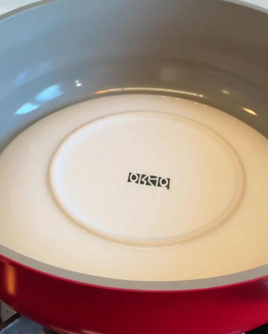 A white plate placed face down inside a red pan to flip a potato crust.