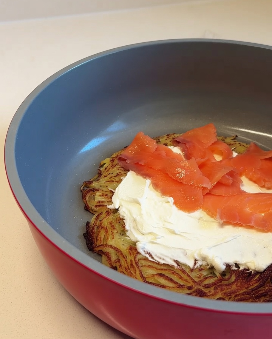 Slices of pink smoked salmon being layered over the cream cheese spread on the potato crust base.