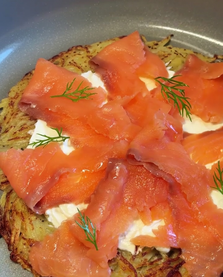 A completed potato and smoked salmon pizza garnished with fresh dill sprigs and red onion pieces.
