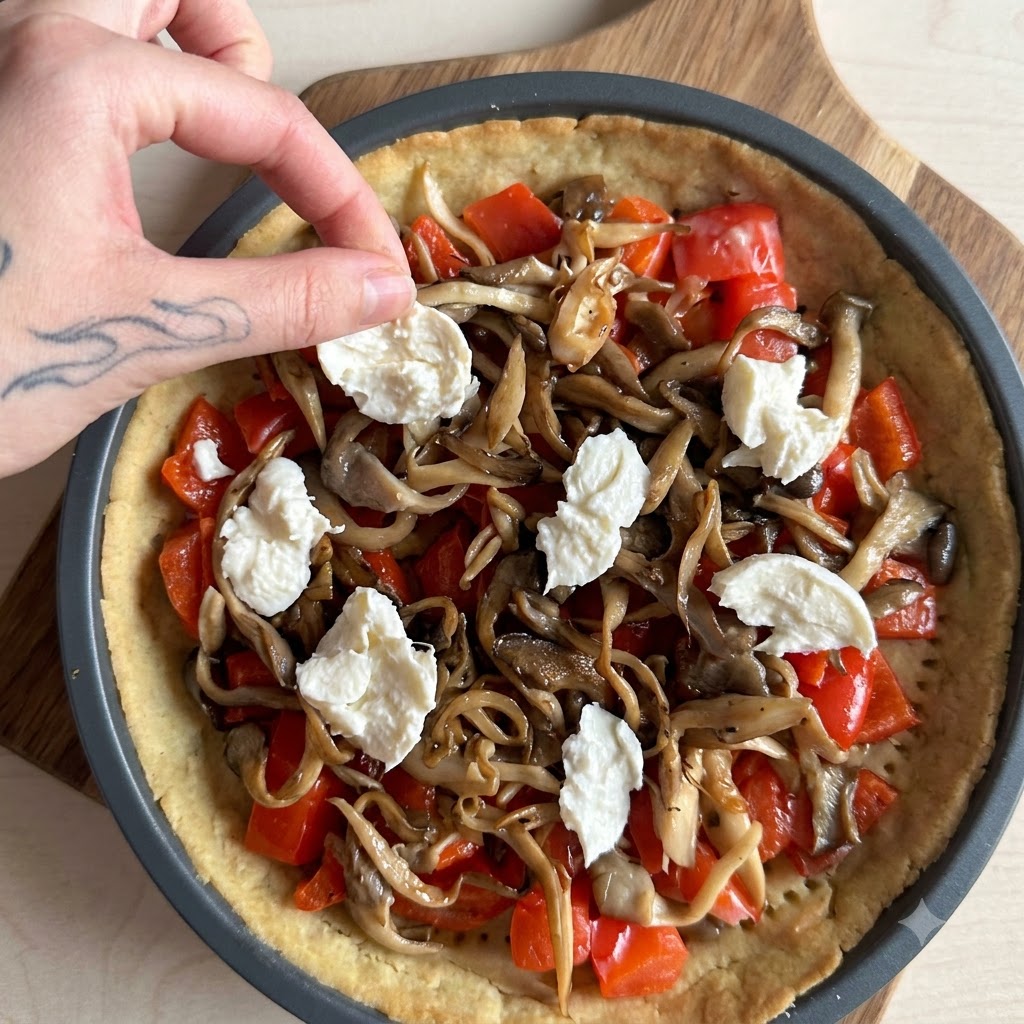 Cream being poured over a pie filled with salmon, mushrooms, and mozzarella.