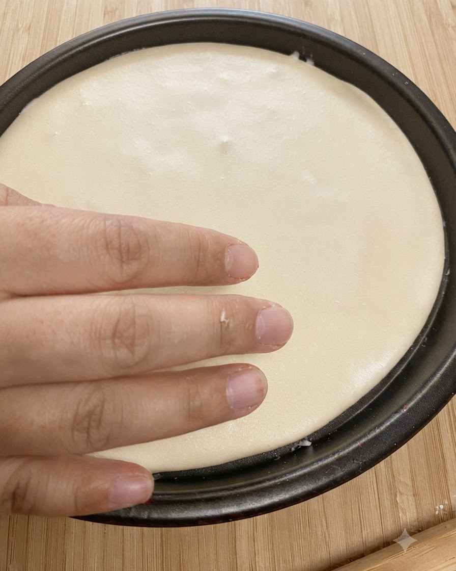 Flattened round dough fitted inside a black baking pan with a hand pressing the edges.